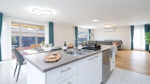 Eine moderne Küche mit Kochinsel, ein Essbereich mit Tisch und Stühlen sowie ein Wohnzimmer mit Sofa und Fernseher.