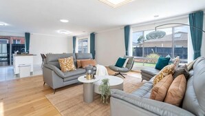 Ein modernes Wohnzimmer mit grauem Sofa, einem Couchtisch und einem Essbereich im Hintergrund.