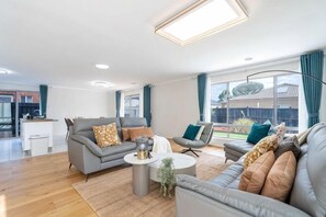 A modern living room with a grey sofa, a coffee table, and a dining area in the background. - Spacious 4B House in PointCook (Point Cook)