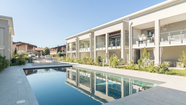 Un hotel moderno con piscina central, mobiliario exterior y un jardín bien cuidado.