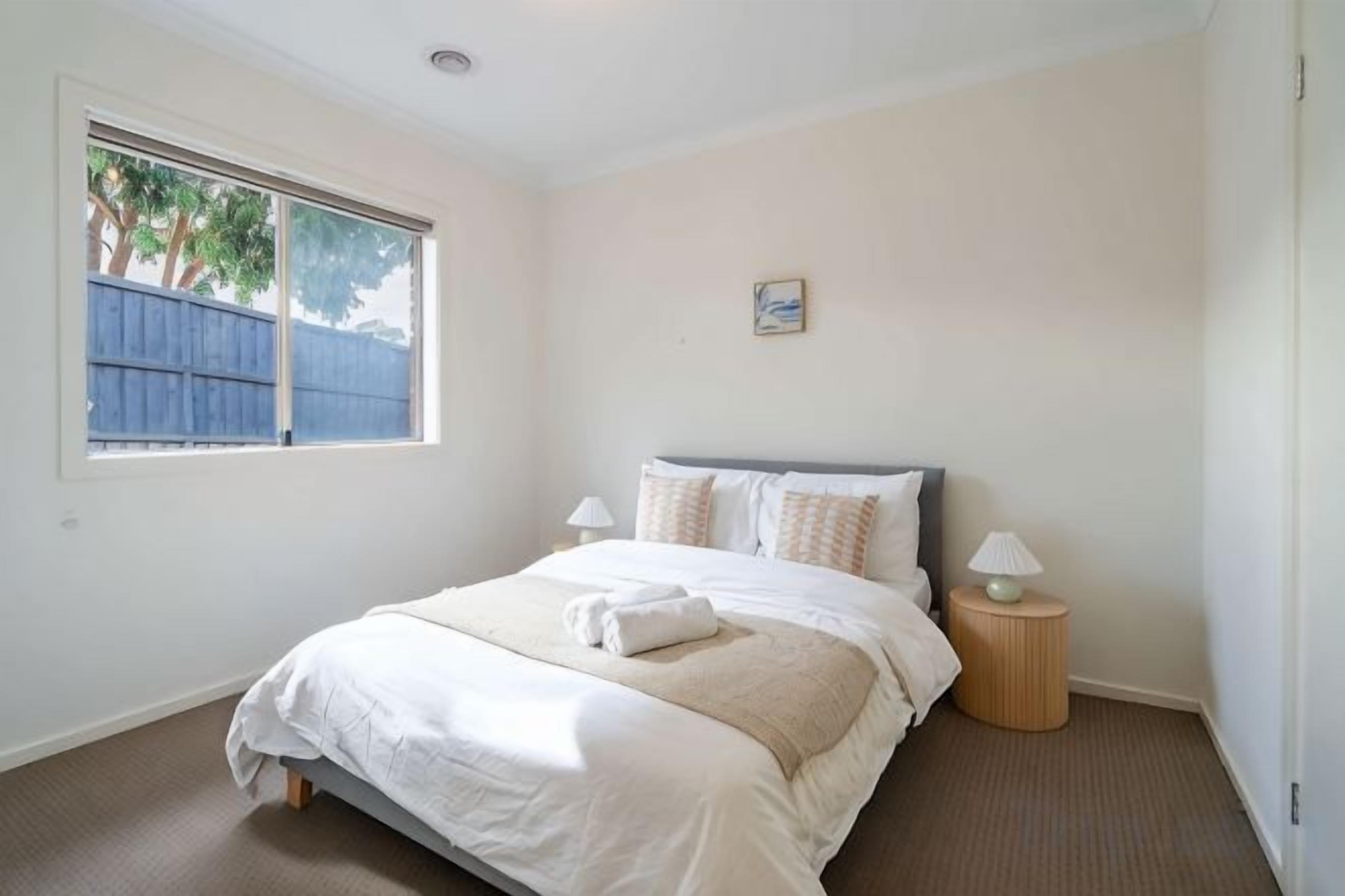 A bedroom with a bed, bedside lamps, a window, and a small picture on the wall.