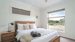 Un dormitorio con una cama de madera, una mesita de noche, una lámpara y una ventana con vistas a zonas verdes.