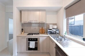 A modern kitchen with a stove, oven, and sink, light wood cabinets, and a window with a view. - Modern 3B2B1C Home in Doreen (Mernda)