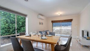 Un comedor con una mesa de madera, cuatro sillas y vistas a la playa a través de amplios ventanales.
