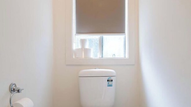 A small bathroom with a toilet, a roll of toilet paper, a window, and a metal container. - Modern 3B2B1C Home in Doreen (Mernda)