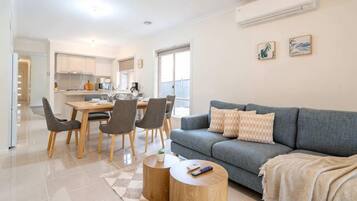 A modern living room with a grey sofa, a coffee table, and a dining area with chairs and a table.