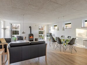 Eine moderne Küche mit Kaminofen, einem Essbereich mit Tisch und Stühlen sowie einer Sitzecke mit einer Couch.