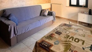Una sala de estar con un sofá, una mesita de centro con diseño de mapa, un radiador, una ventana con cortinas y un armario blanco.