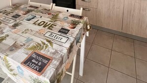 Una cocina con armarios blancos, una estufa a gas, un fregadero y una mesa con mantel decorado con motivos de jardín.