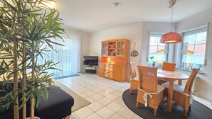 A living room with a television, wooden cabinet, dining table with chairs, and a potted plant. - Vacation home Meertraum - Holiday home Meertraum in Neßmersiel modern with beautiful (Dornum)