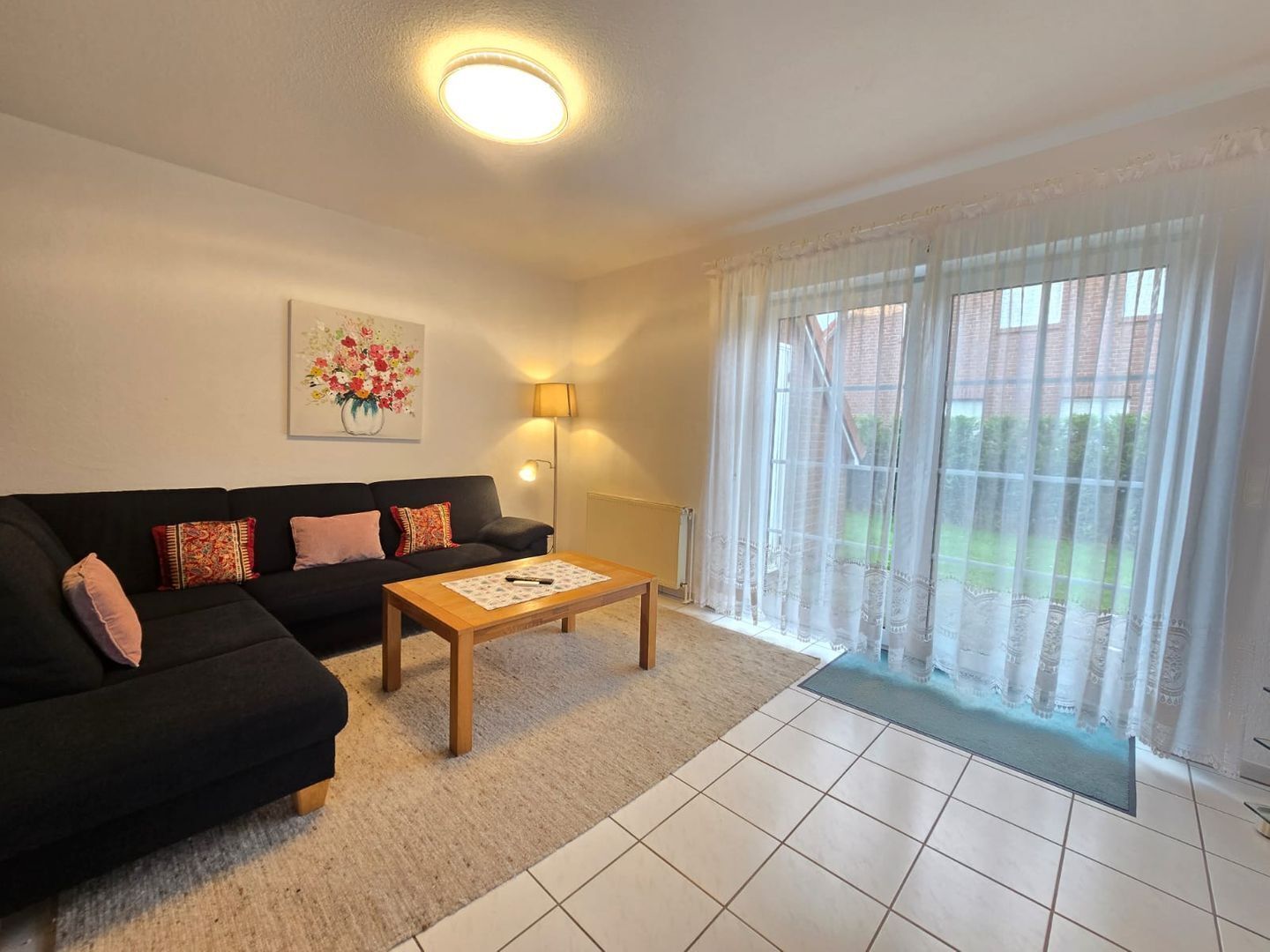 A living room with a sofa, a coffee table, a lamp, and a large window with curtains.
