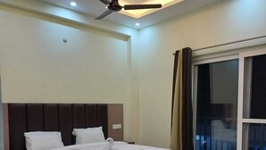 A modern bedroom with a large bed, a ceiling fan, and a view of the outside through a large window. - Sampati Homestay (Rishikesh)