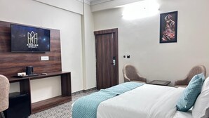 A hotel room with a bed, a desk, a chair, a TV, and a door. - Sampati Homestay (Rishikesh)