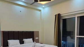 A modern bedroom with a large bed, a ceiling fan, and a large window with curtains. - Sampati Homestay (Rishikesh)