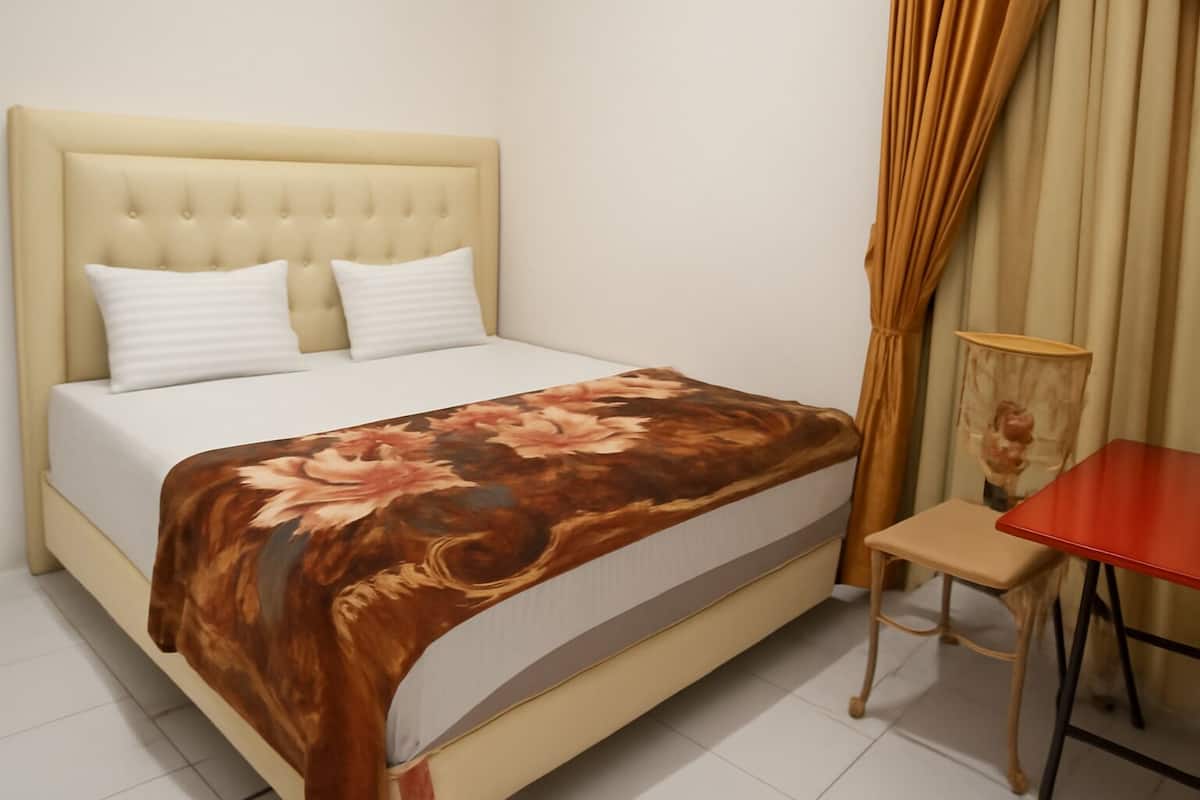 Ein Schlafzimmer mit einem Bett, zwei Kissen, einer blumigen Tagesdecke, einem kleinen Tisch und Vorhängen.