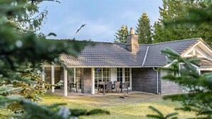 Ett modernt hus med en täckt uteplats, en tegelbeklädd skorsten och en gräsmatta.