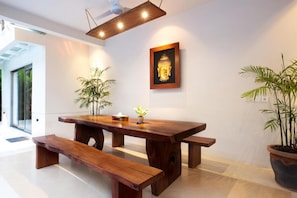 A wooden dining table with benches, a Buddha statue, and potted plants in a modern interior.