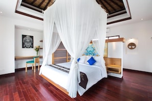 A bedroom with a canopy bed, a wooden chair, a small table, and a wall with a Buddha painting.