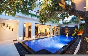 A modern pool area with a clear pool, surrounded by a white building with indoor seating and greenery. - Sunset Paradise Villa Jimbaran 3003 (Kedonganan)