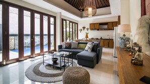 A spacious living area with a large sofa, a coffee table, and a dining table. There is a kitchen in the background with wooden cabinets and a large vase. - Marijo Villa 2BR Private Pool Mins to Central Ubud (Ubud)