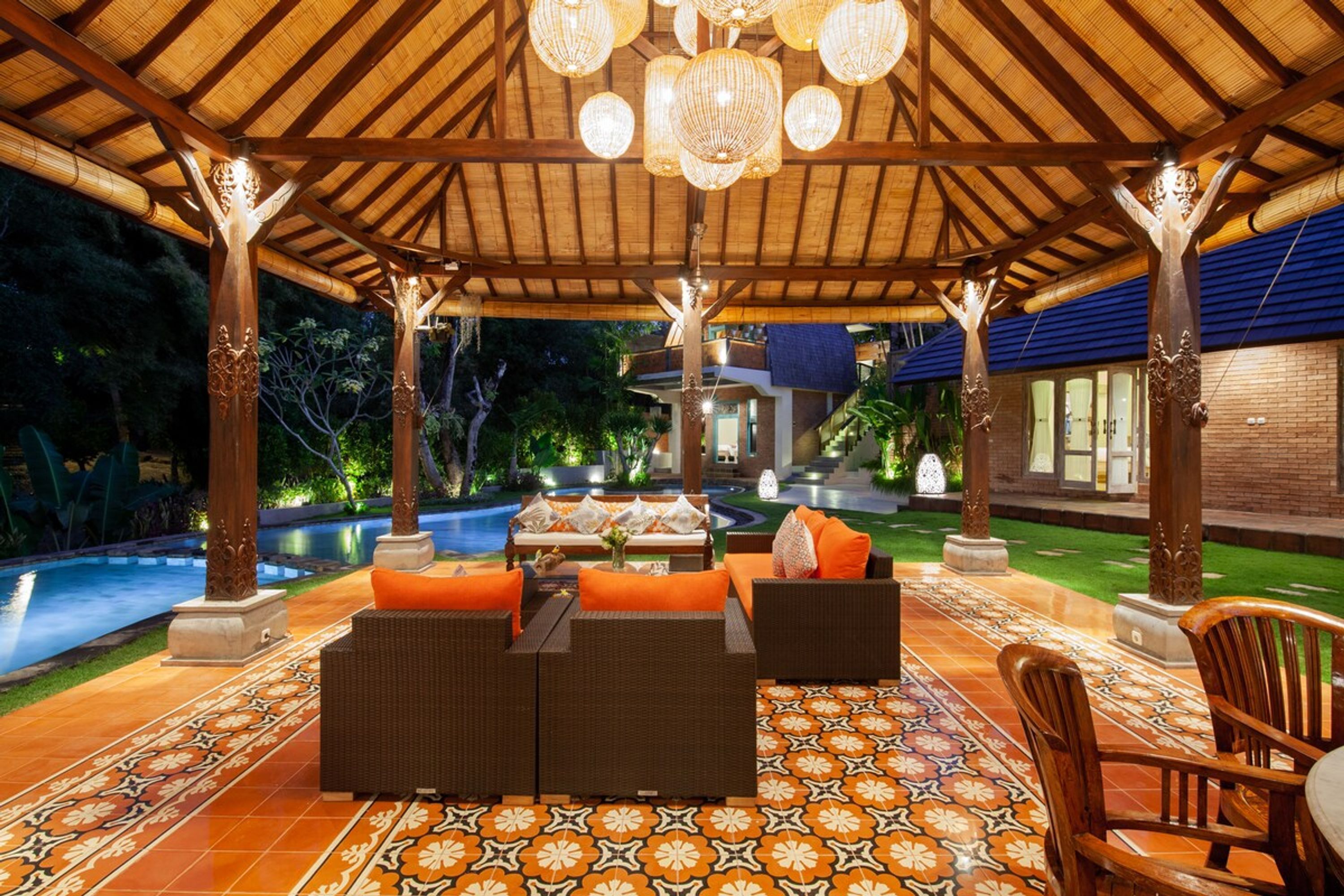A covered outdoor seating area with wicker furniture, a pool, and a patterned floor.