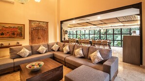 A modern living room with a sectional sofa, a coffee table, and a dining area visible through a large window. - SPV Nusa Dua Luxury Traditional Design Nusa Dua (Nusa Dua)