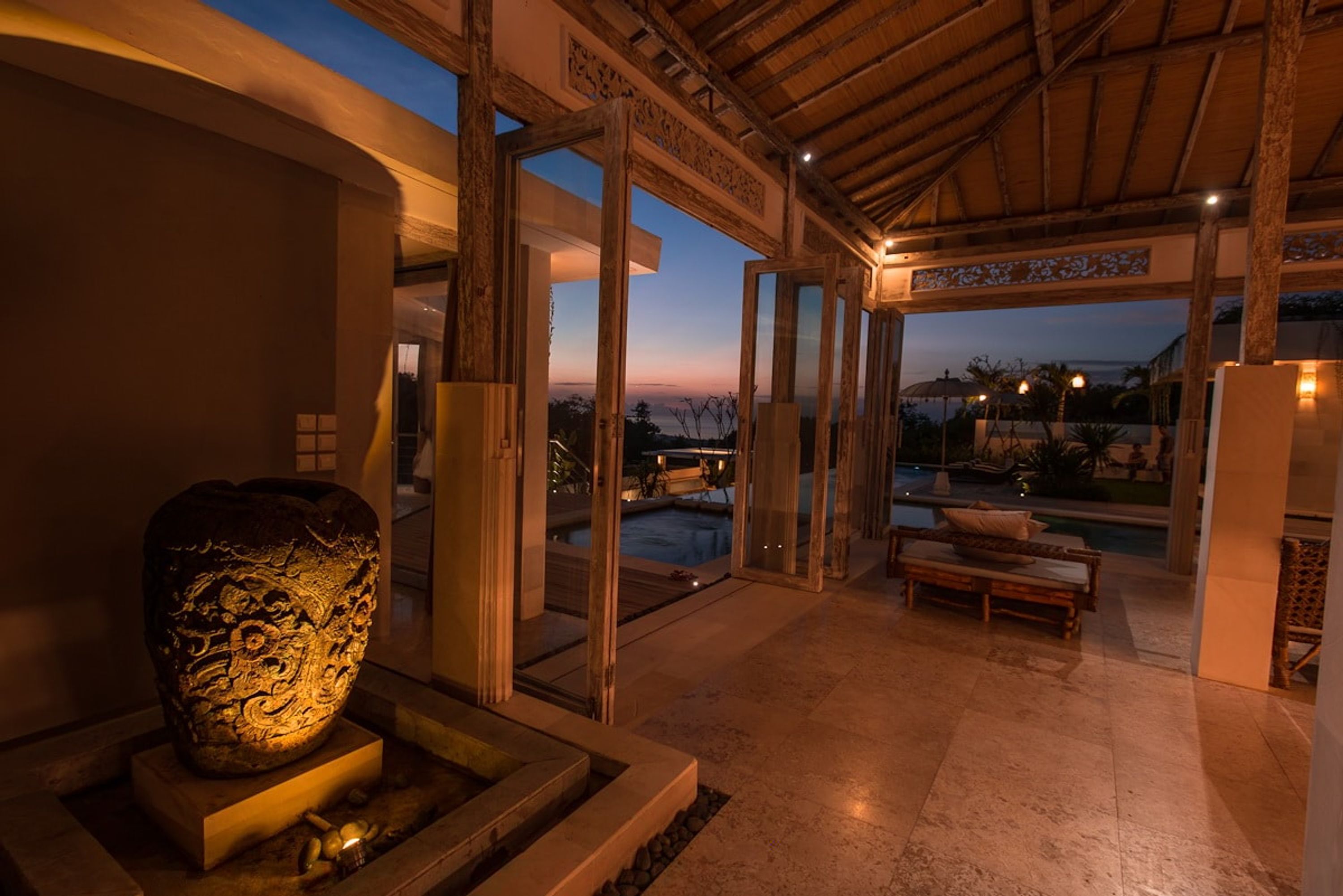 Amplio espacio interior con una gran escultura de piedra, una piscina y una zona de estar con vistas al exterior.