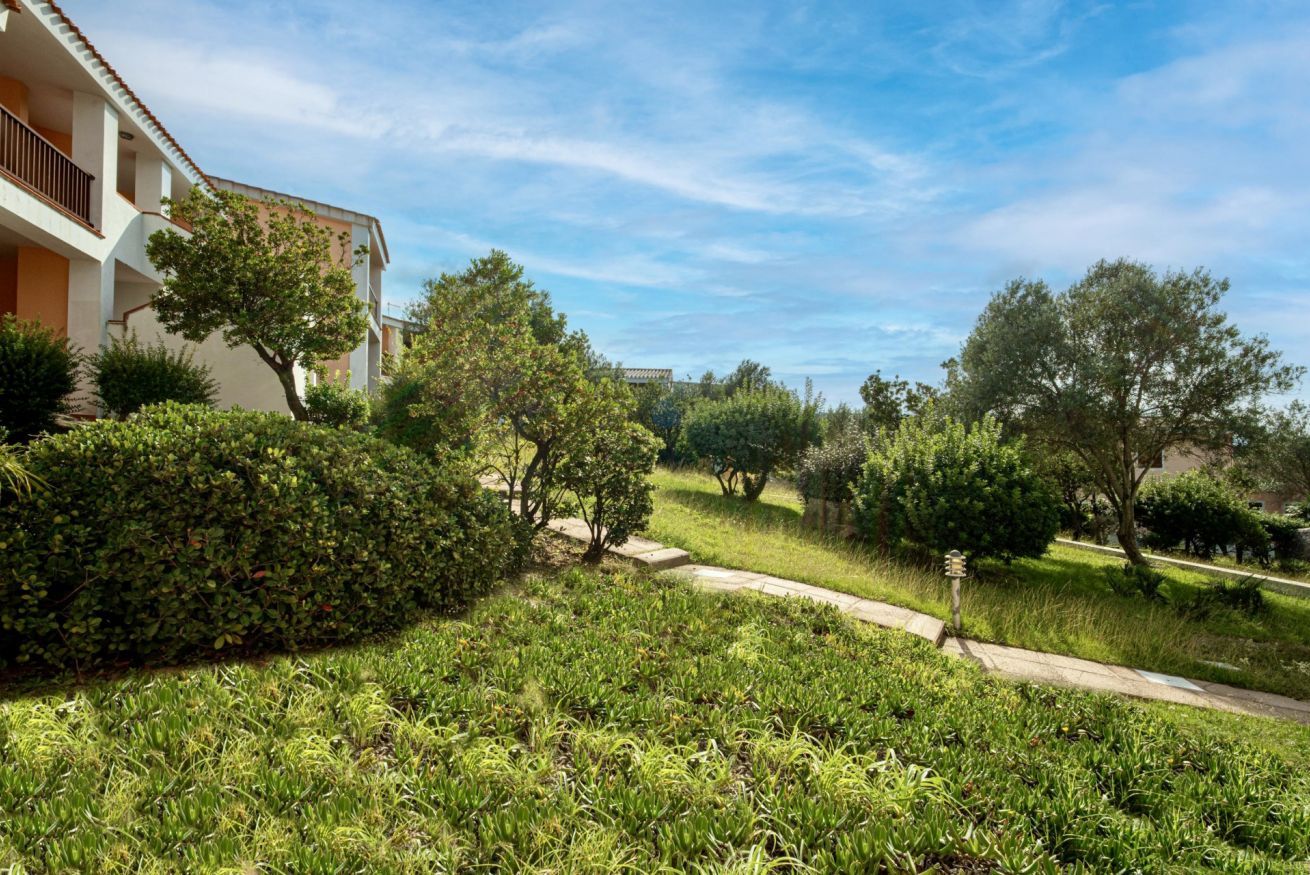 Zona residencial con un edificio que tiene balcones, rodeada de vegetación y árboles bien cuidados.