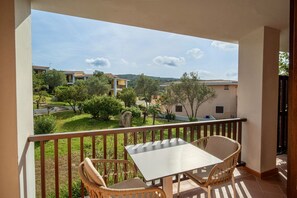 Ein Balkon mit Tisch und Stühlen, der auf einen Innenhof mit Grünflächen und Gebäuden blickt.