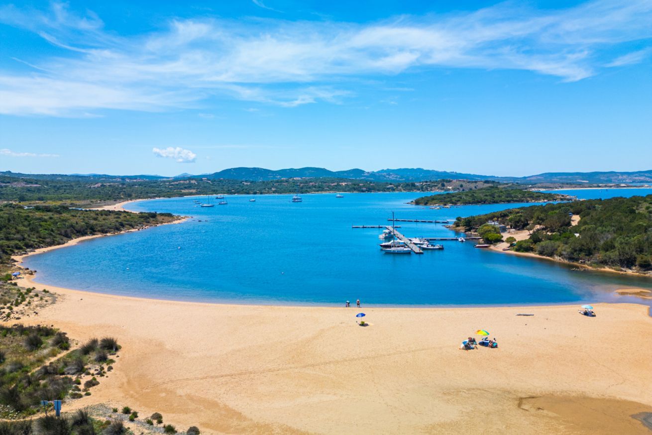A coastal beach with boats, clear blue water, and a sandy shore.