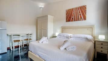 A hotel room with a bed, white curtains, a desk with chairs, a wardrobe, and a wall-mounted artwork.