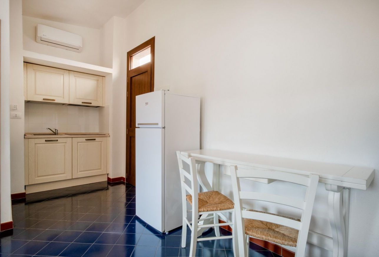 Una cucina con mobili bianchi, un frigorifero bianco e un tavolo da pranzo con due sedie in vimini.