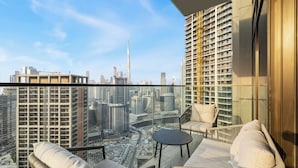Ein hoher Balkon mit Korbmöbeln, Glasgeländer und Blick auf die Stadt.