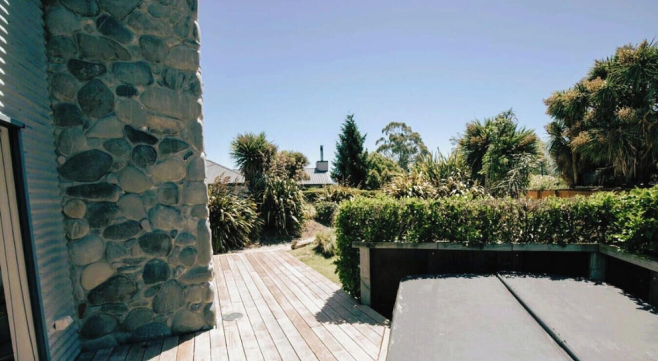 A stone wall, a wooden deck, and a garden with various plants and trees.
