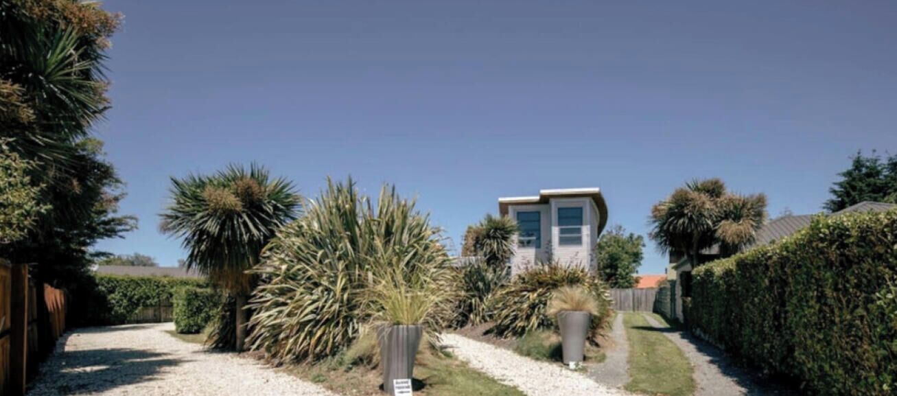 Une maison moderne avec une allée en gravier, entourée de haies bien entretenues et de diverses plantes.
