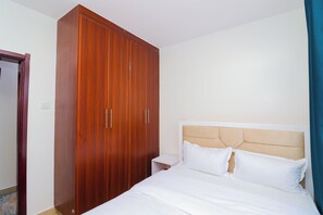 Un dormitorio con un armario de madera, una cama con ropa de cama blanca y una mesita de noche.