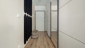 Un pasillo estrecho con suelo de madera, una puerta al final y un pequeño otoman.