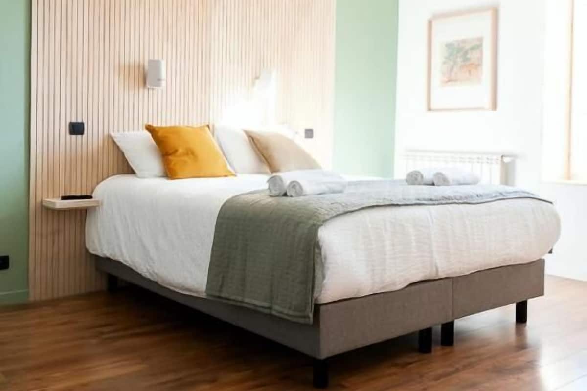 Een moderne slaapkamer met een houten hoofdbord, een bed met wit beddengoed en een groene plaid, en een houten vloer.