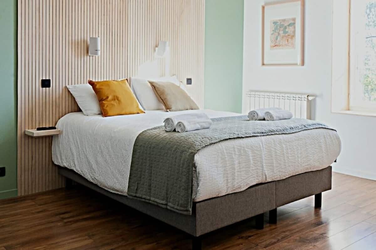 Een moderne slaapkamer met een houten lattenkap, een bed met een grijs-witte deken en een houten vloer.