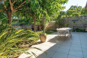 An outdoor patio area with a stone wall, a table with chairs, and a variety of plants.
