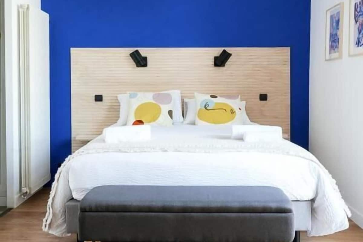 Een moderne slaapkamer met een blauwe accentmuur, een houten hoofdbord en een grijze bank.