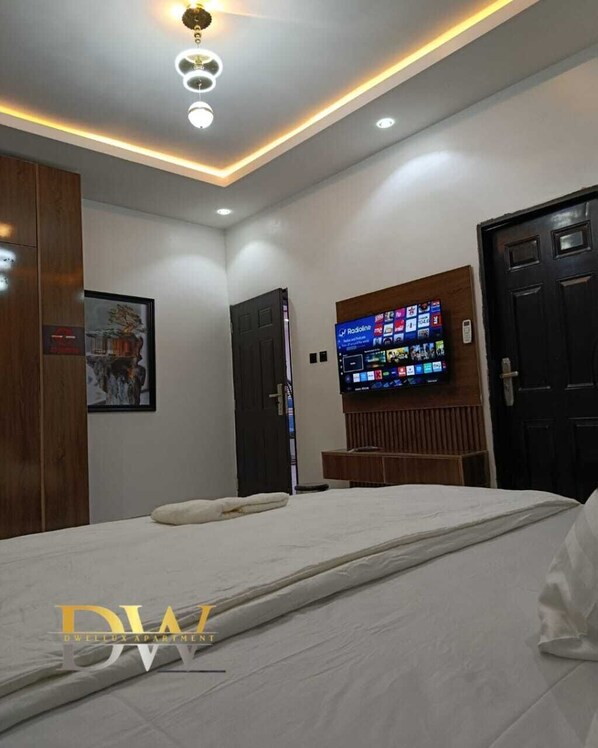 A modern bedroom with a bed, a mounted TV, and a ceiling light fixture. - Dwellux Apartments  (Abuja)