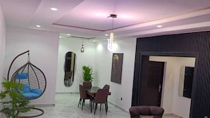 A modern living room with a sofa, a hanging chair, a dining area with chairs and a table, and a large mirror on the wall. - Dwellux Apartments  (Abuja)