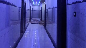 A hallway with a blue-lit ceiling, tiled floor, and doors on both sides. - Hotel Radhe Krishna (Khatoo)