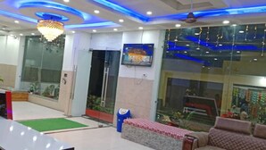A lobby with a chandelier, seating area, and a television screen. - Hotel Radhe Krishna (Khatoo)