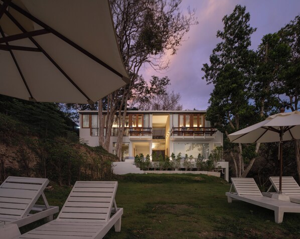 Una casa moderna de dos pisos con balcón, césped y sillones de descanso.