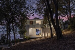 A modern two-story house with a glass facade, surrounded by trees and a view of the sea. - Pebble Lanta - Seaview Stay (Ko Lanta)