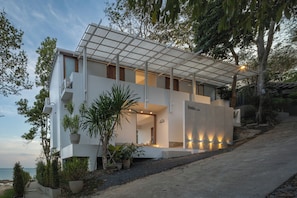 A modern two-story building with a flat roof, large windows, and a balcony. There are potted plants and a pathway leading to the entrance. - Pebble Lanta - Seaview Stay (Ko Lanta)