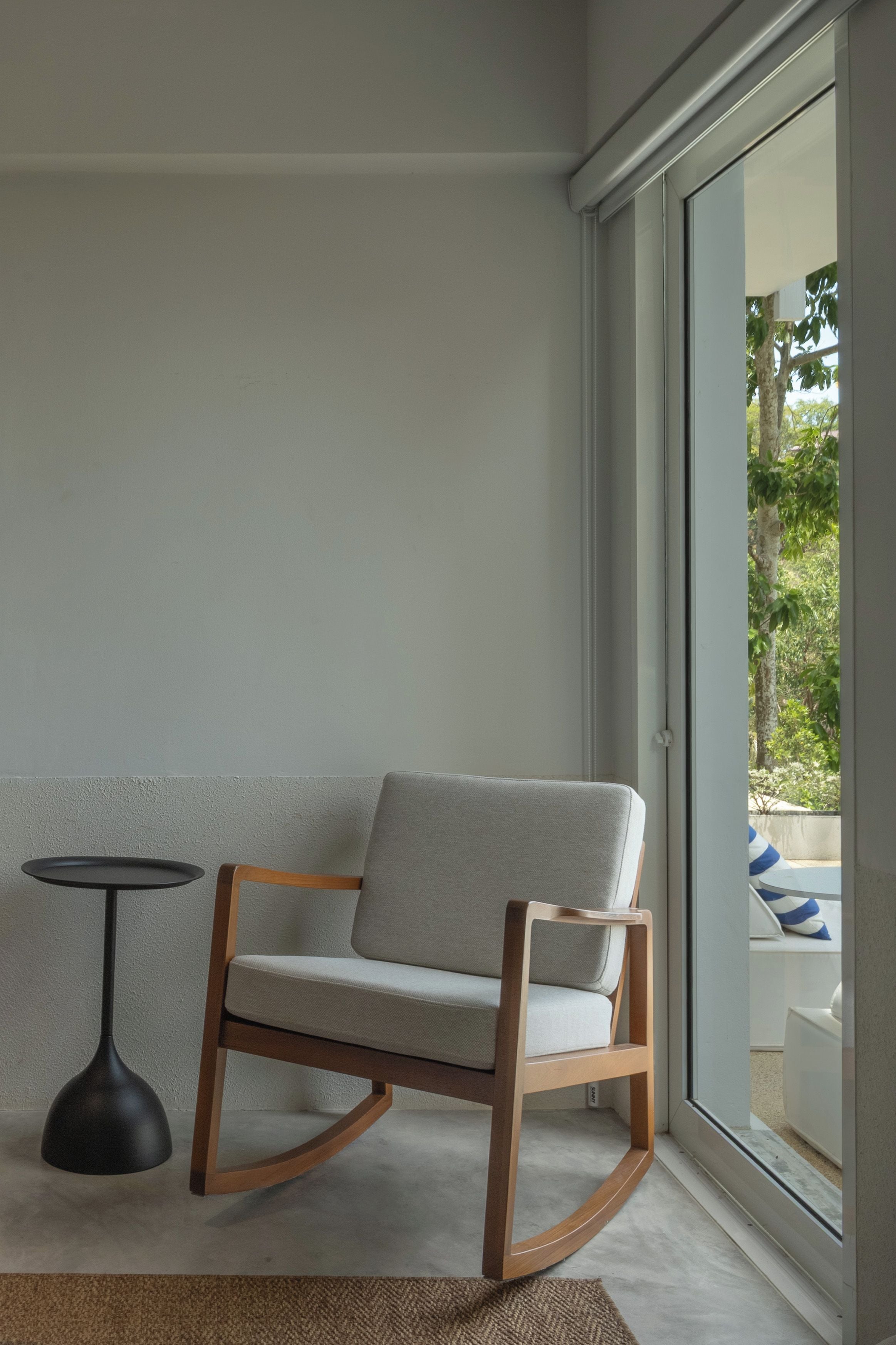 A modern room with a rocking chair, a small round table, and a view of the outdoors through a glass door.
