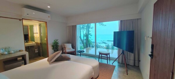 Habitación de hotel con una cama grande, un televisor en un mueble, una mesita y vista al mar.
